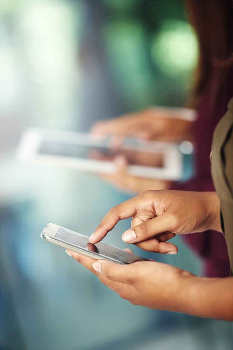 Hands in focus in foreground using a smartphone, hands out of focus in background using a tablet